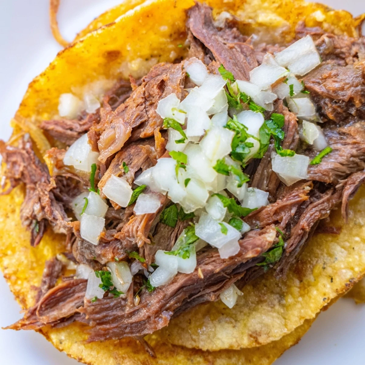 Freshly prepared Slow Cooker Beef Birria Tacos sit crisped in a skillet, garnished with cilantro and onions, ready for dipping into a steaming bowl of rich consommé. 