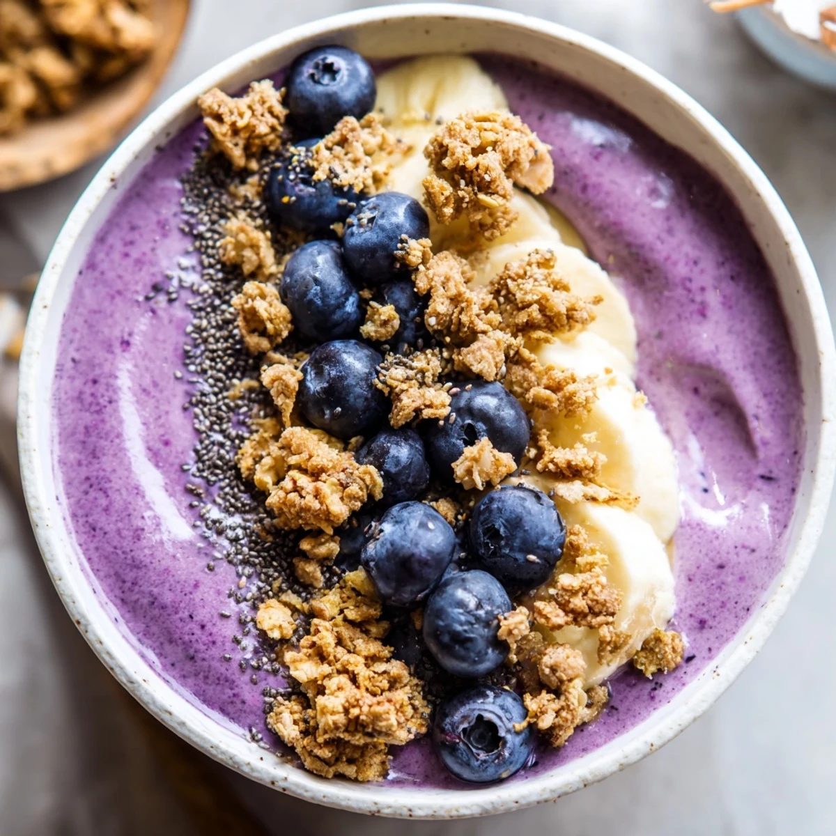 Thick lemon blueberry smoothie bowl topped with crunchy granola, fresh berries, and coconut flakes.