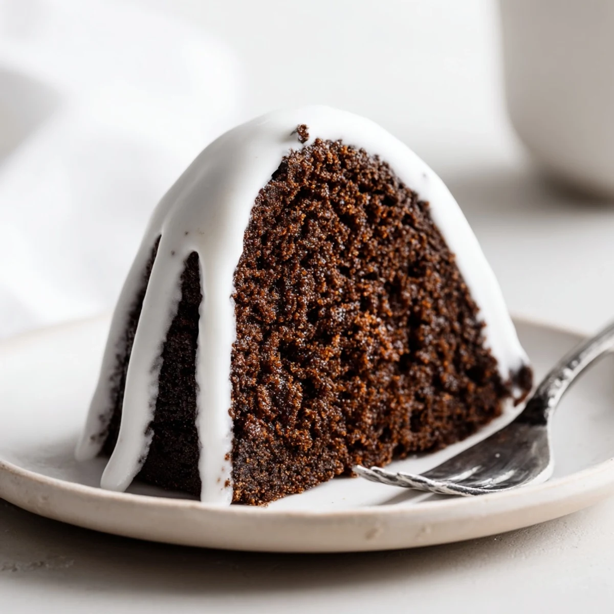A moist Gingerbread Spiced Bundt Cake drizzled with sweet vanilla glaze, served alongside a steaming mug of coffee on a festive table.