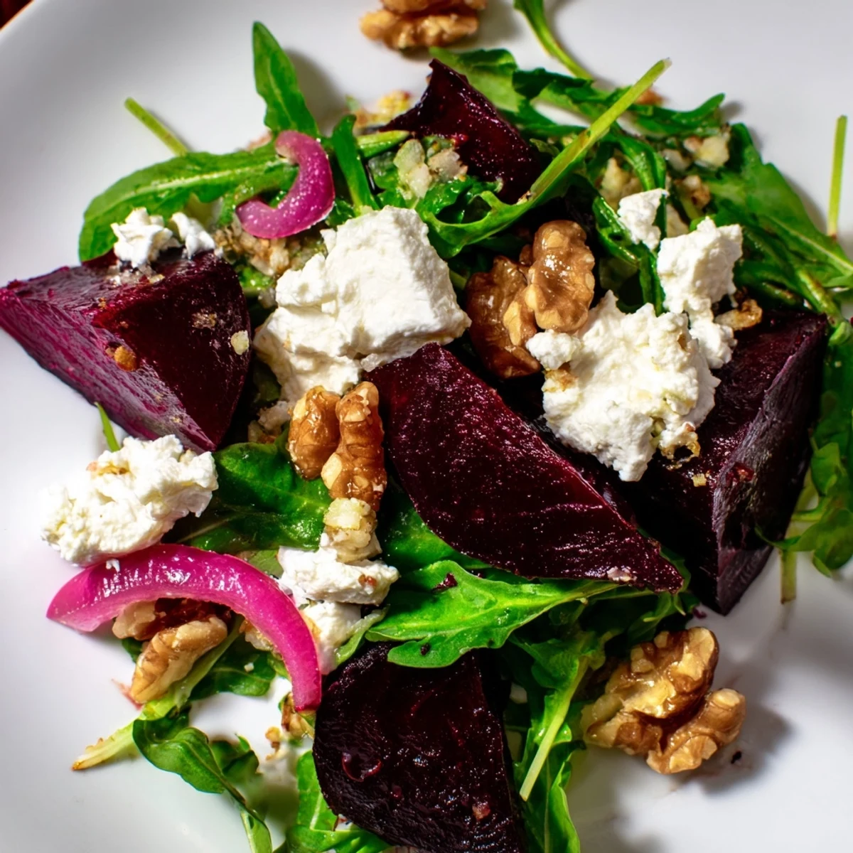 Roasted Beet Salad with arugula, sliced red onion, and crumbled feta topped with toasted walnuts on a platter.