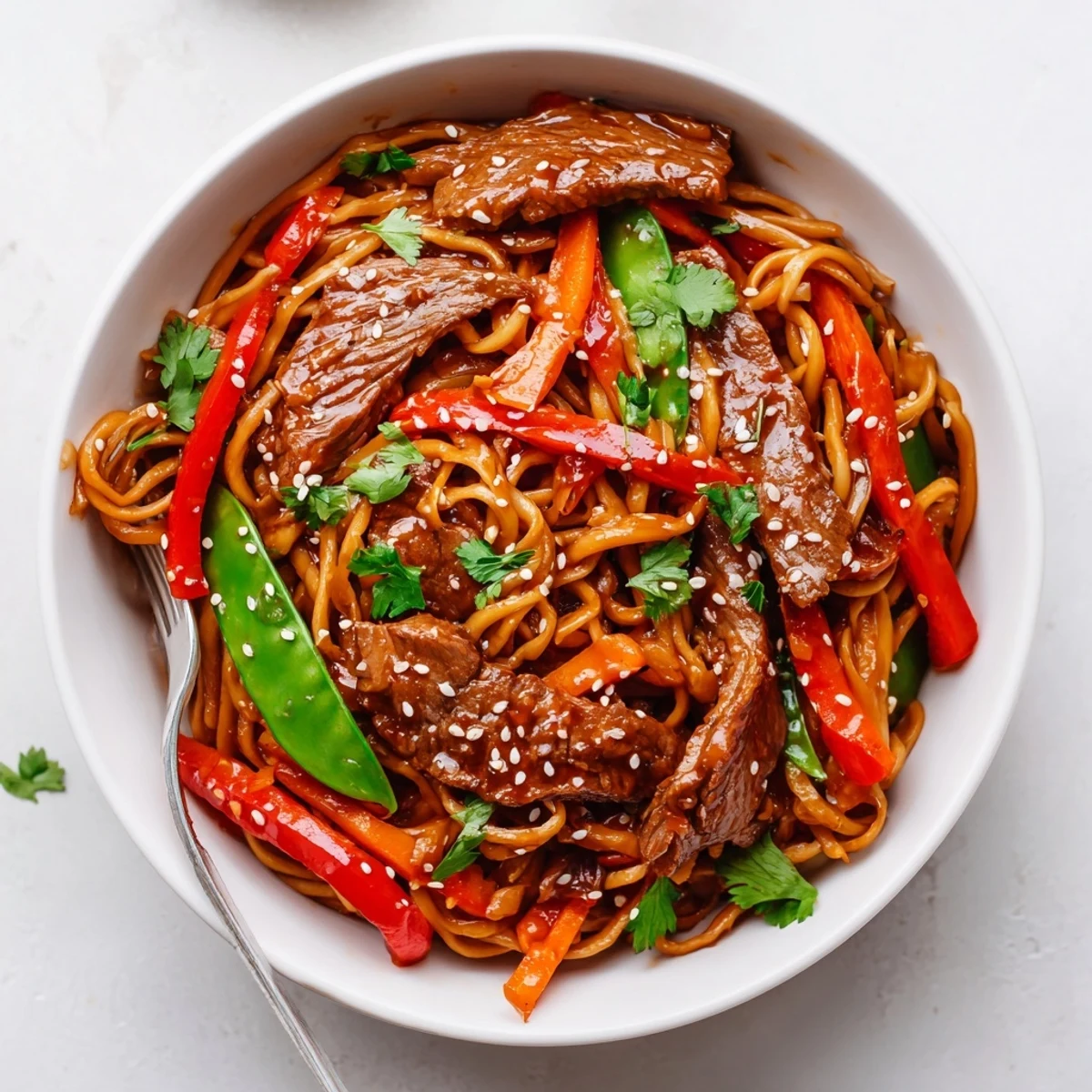A close-up of Spicy Beef Noodles garnished with sesame seeds, cilantro, and vibrant red bell peppers.