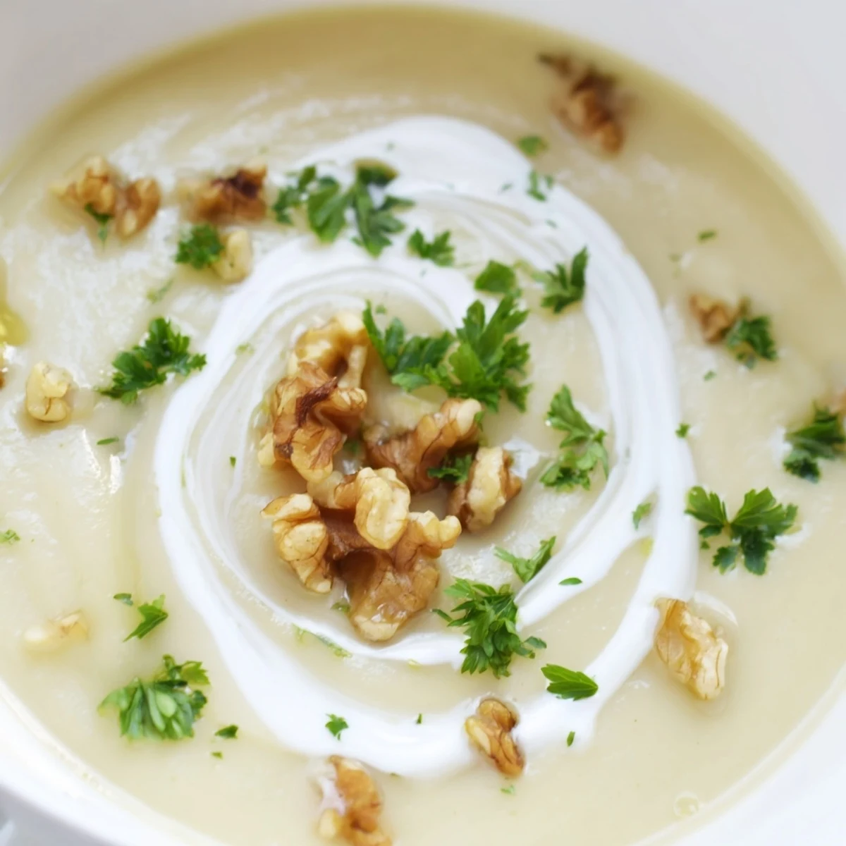 A bowl of Creamy Parsnip and Pear Soup with Walnuts topped with toasted nuts, beside crusty artisan bread.