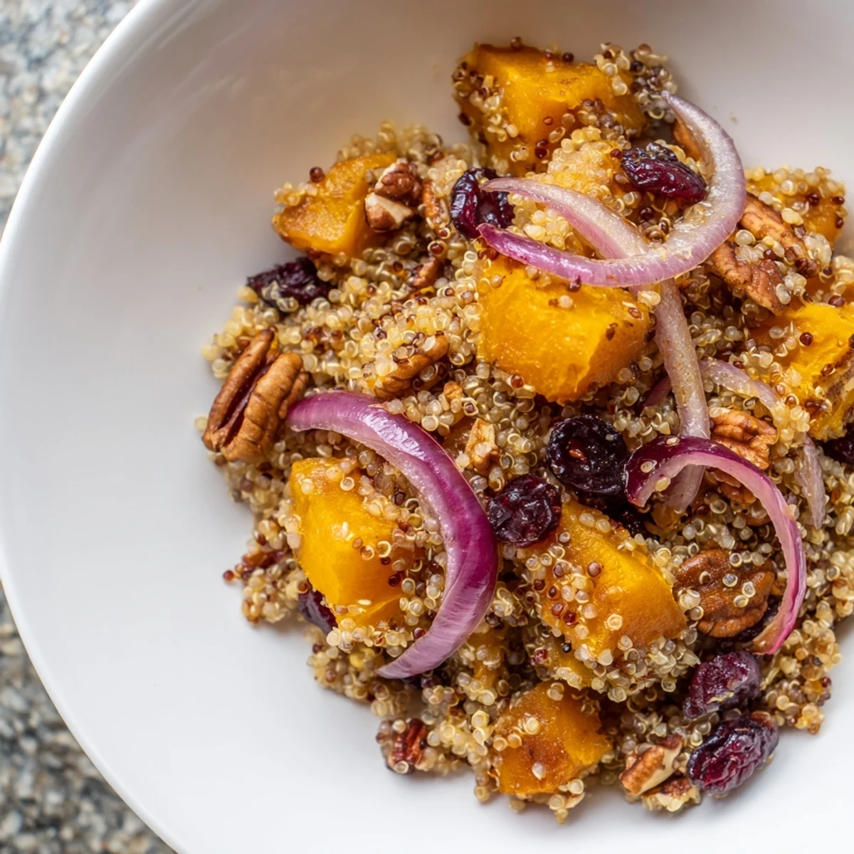 A large serving bowl of warm quinoa salad with roasted squash, cranberries, and wilted spinach, ready to enjoy.
