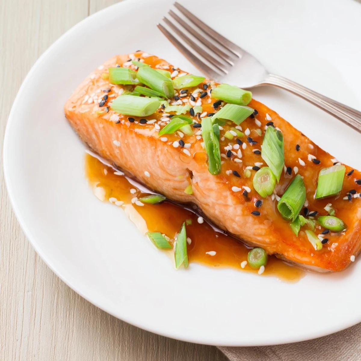 Golden baked salmon fillets coated in a sticky orange ginger glaze, garnished with sesame seeds and green onions on a white plate.