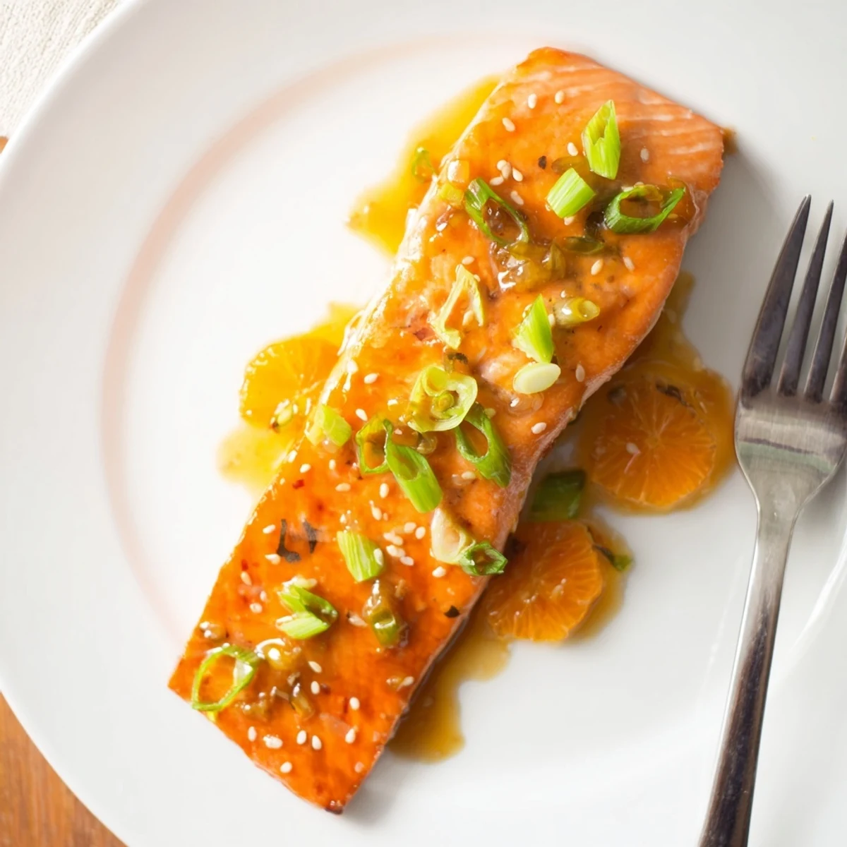 A close-up of glazed baked salmon with orange slices, showing flaky texture and a vibrant orange-ginger sauce drizzle.