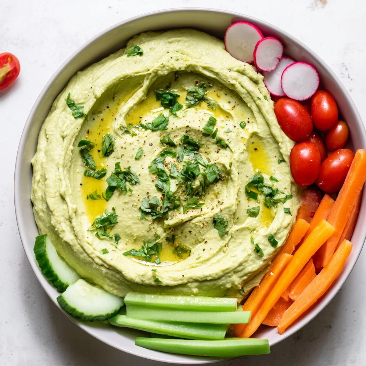 A vibrant serving platter features creamy avocado hummus topped with cilantro and a colorful array of crisp vegetable crudités.