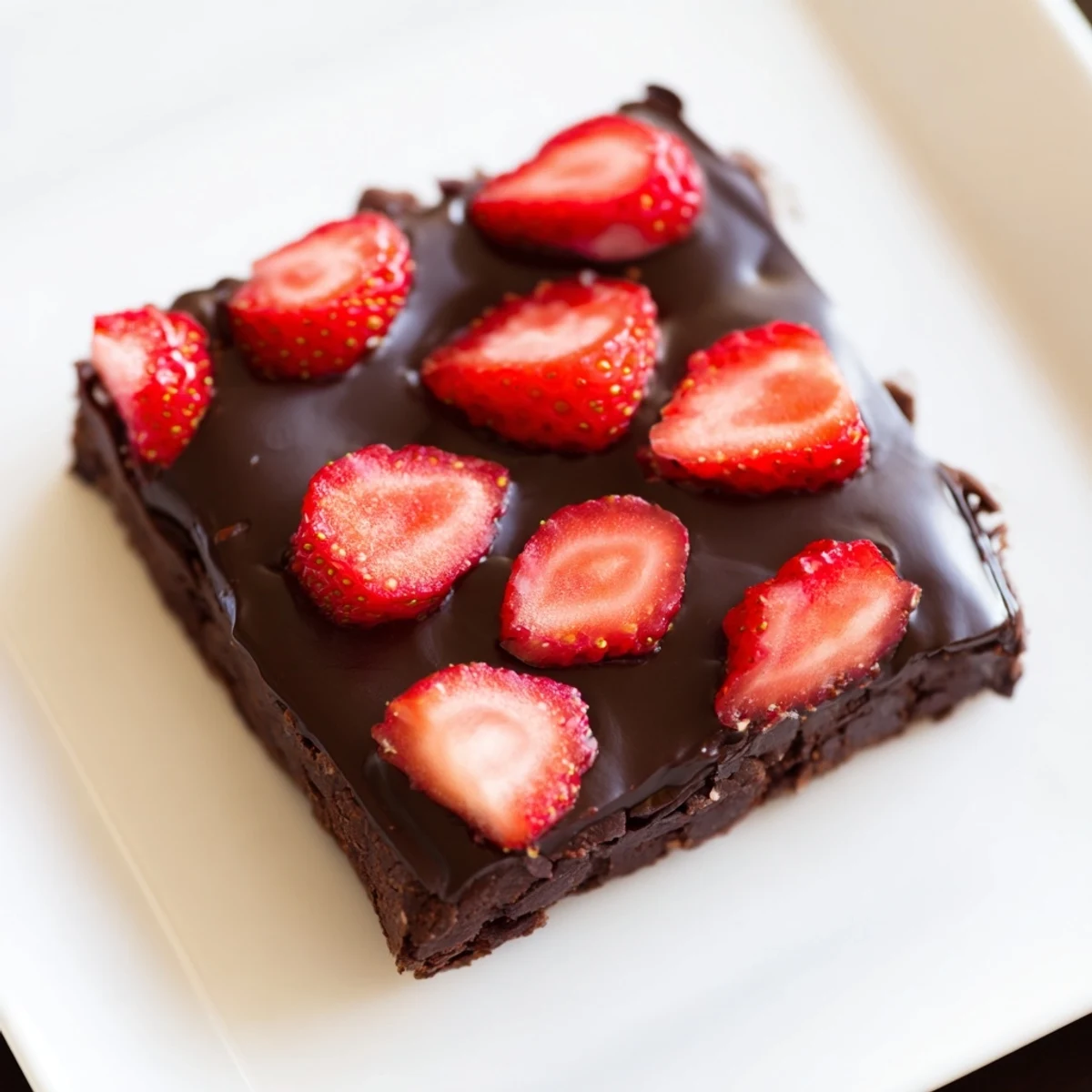 A close-up view of Chocolate Covered Strawberry Brownies squares with glossy ganache, juicy red berries, and fudgy edges on a marble counter.