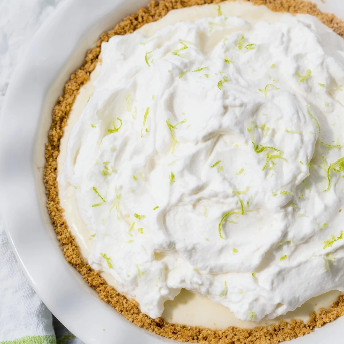 The tangy, refreshing Key Lime Pie with Whipped Cream Topping is served on a rustic plate, ready to enjoy.