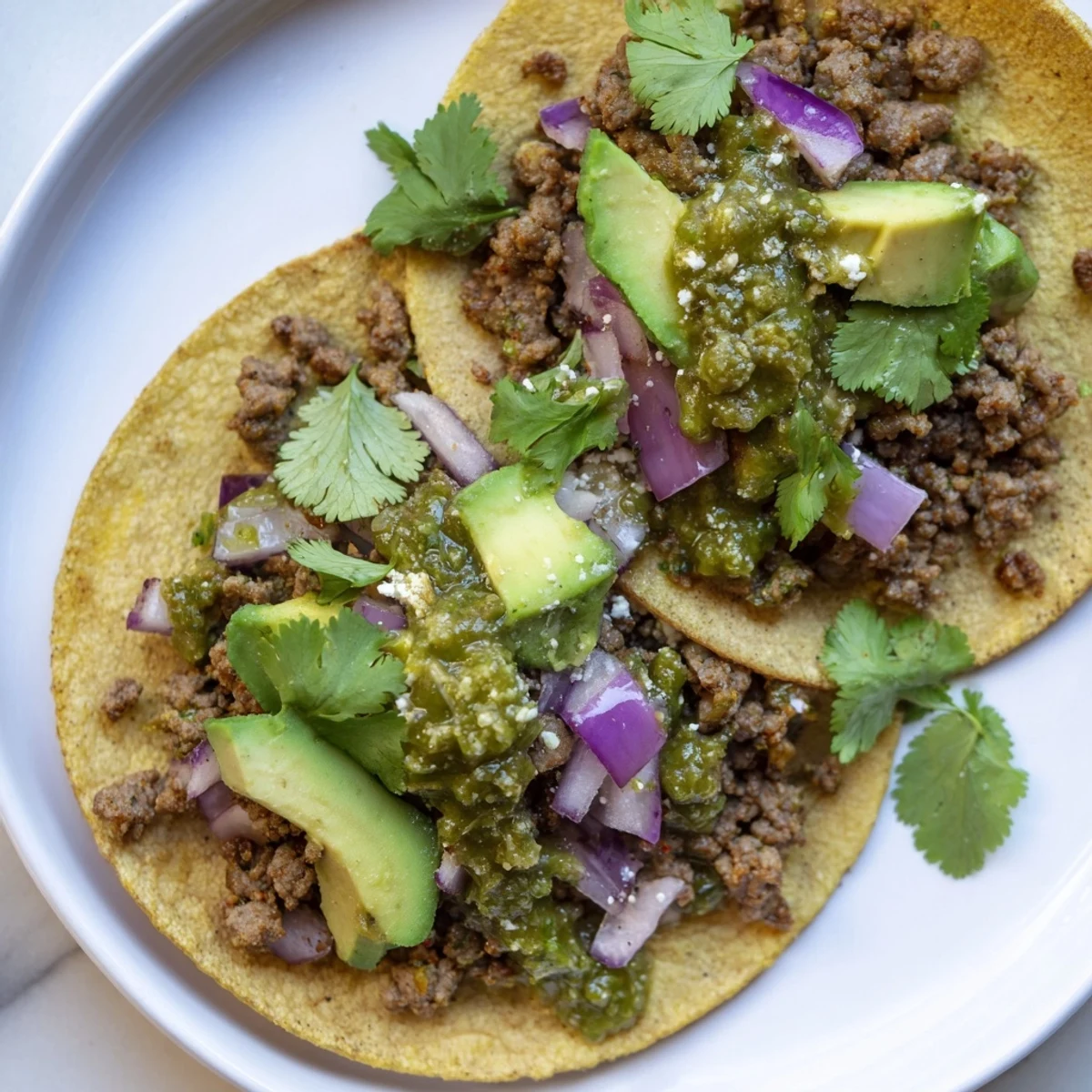 Steamed tomatillos and fresh cilantro blend into a zesty salsa verde, spooned over seasoned, spicy beef tacos with avocado slices.  