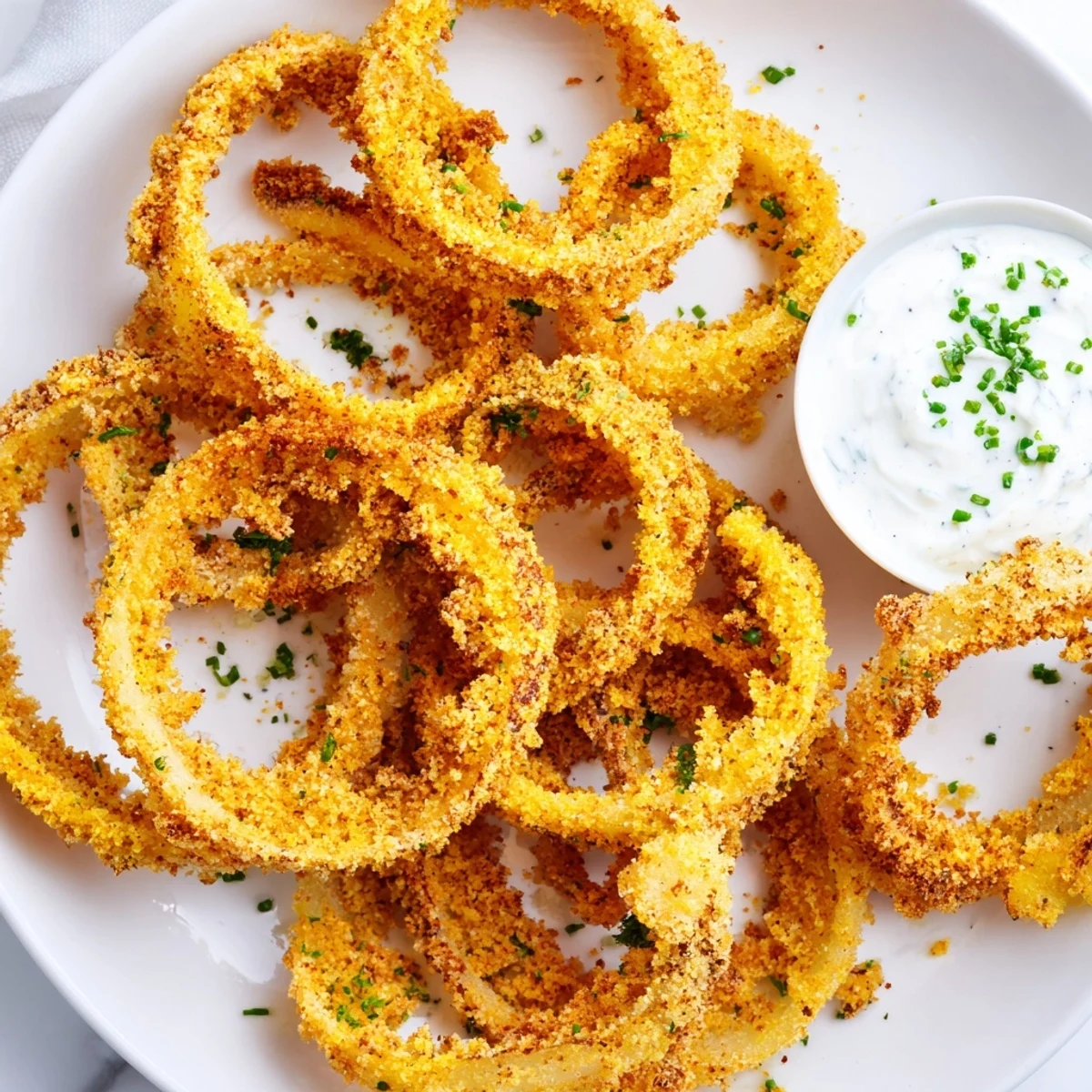 Crispy Baked Onion Rings with Ranch stacked on a plate, showcasing golden-brown panko coating next to a creamy dip bowl.