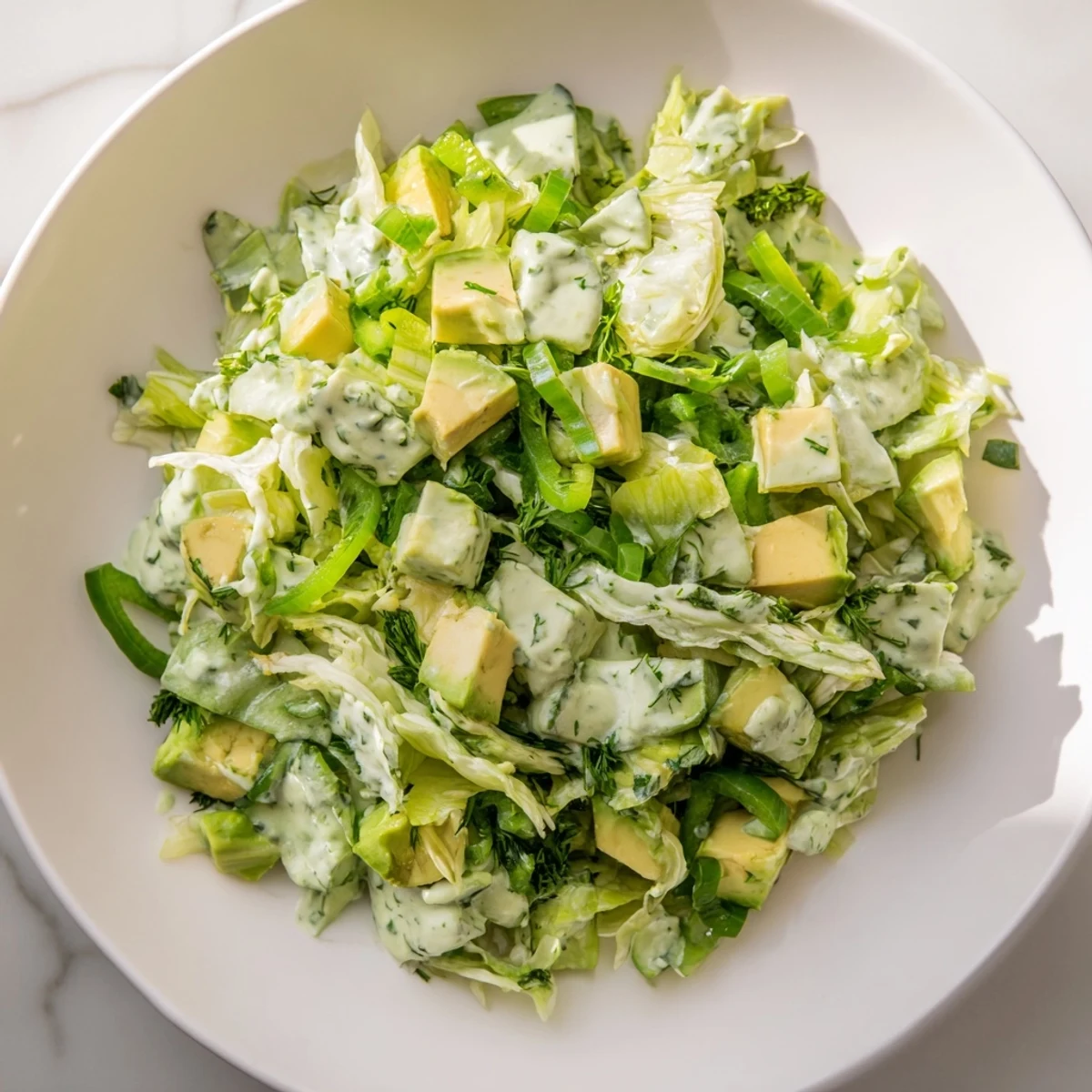 Creamy diced avocado and crisp romaine lettuce tossed in tangy Green Goddess dressing in a vibrant bowl.