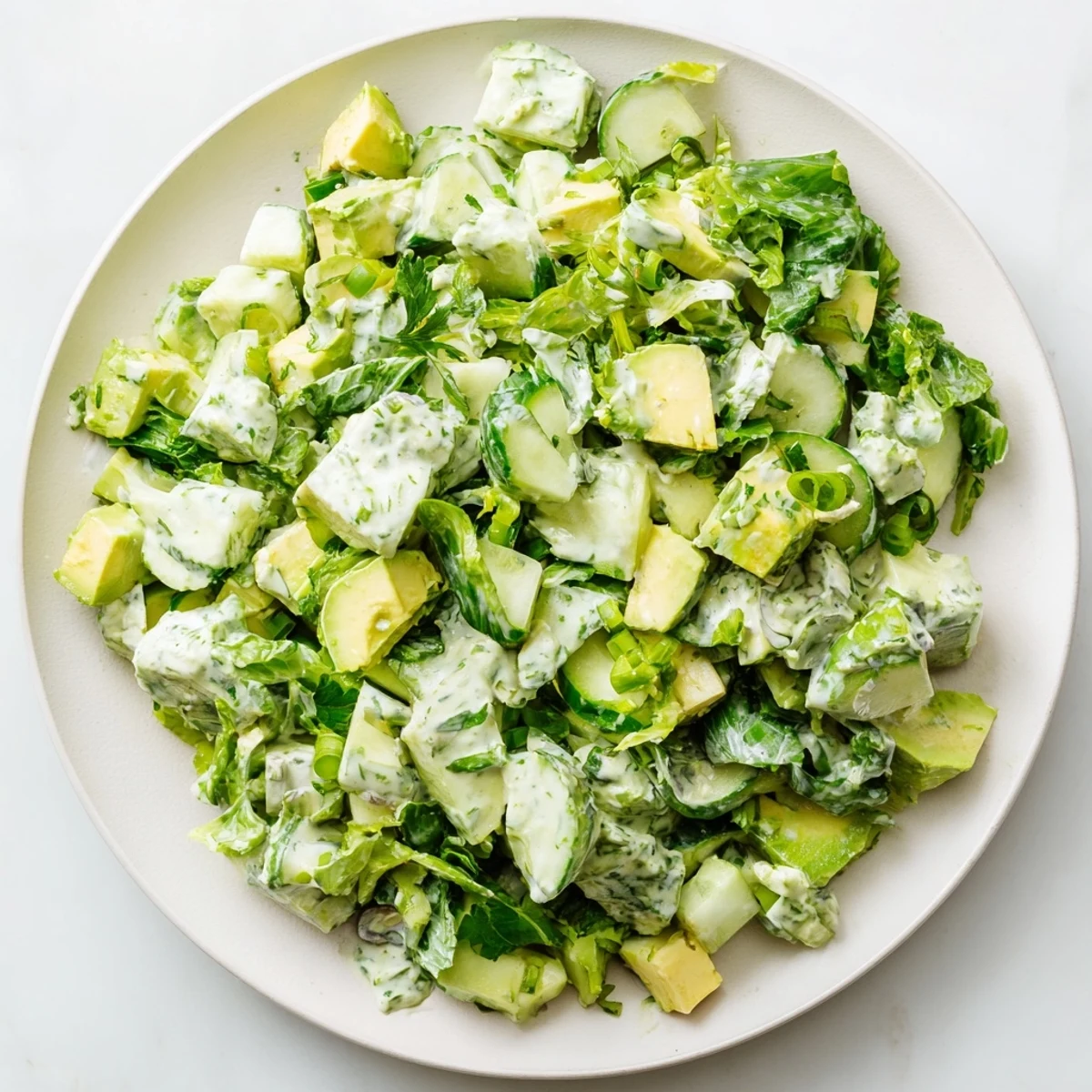 Serving suggestion for Green Goddess Salad with Avocado and Cucumber in a white bowl, topped with extra herbs and a lemon wedge.