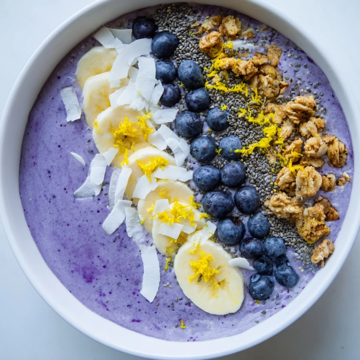 Bright Lemon Blueberry Smoothie Bowl topped with crunchy granola, fresh blueberries, and banana slices, served in a white bowl for a healthy breakfast. 