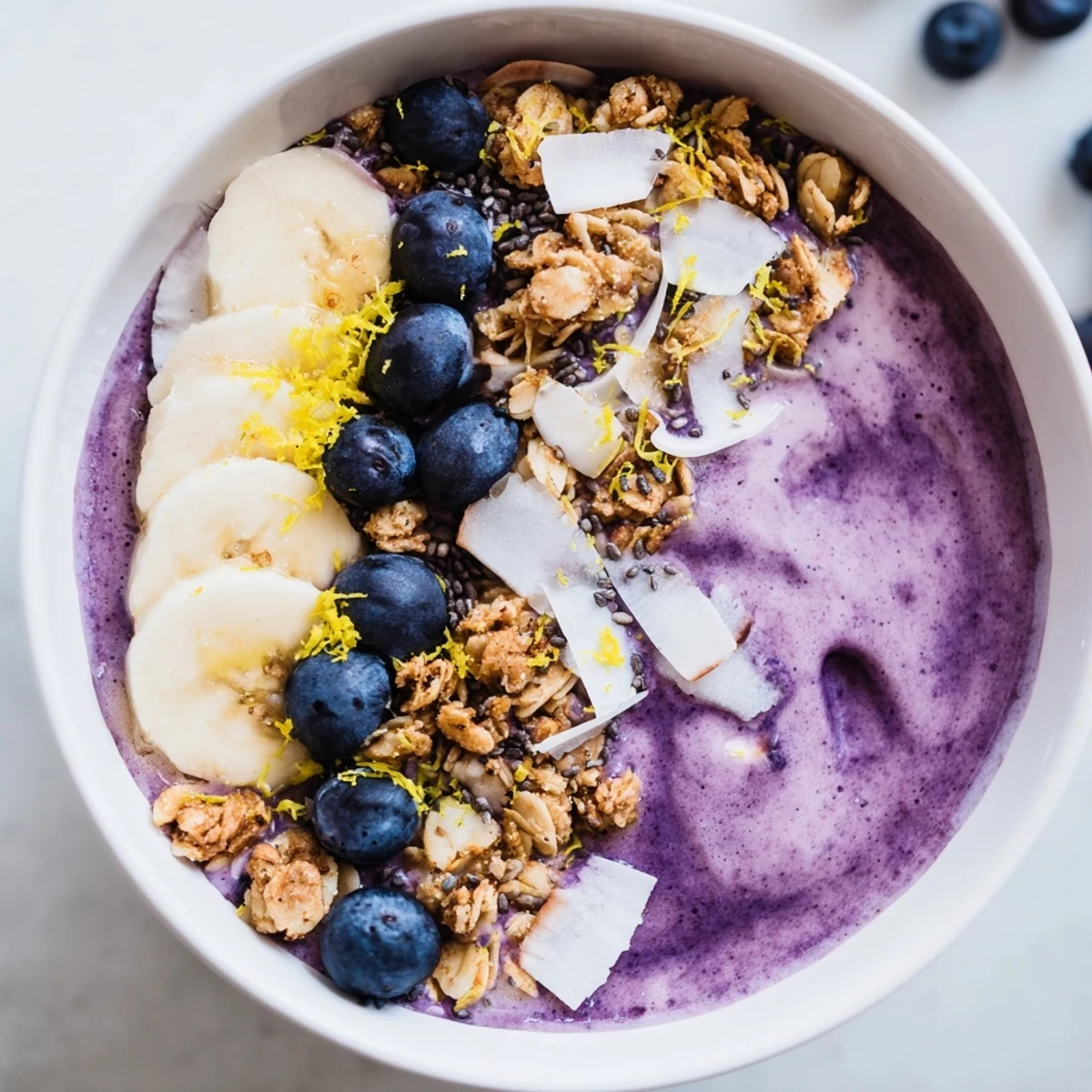 A close-up of a thick Lemon Blueberry Smoothie Bowl with vibrant purple hue, coconut flakes, and chia seeds for added texture and nutrition. 