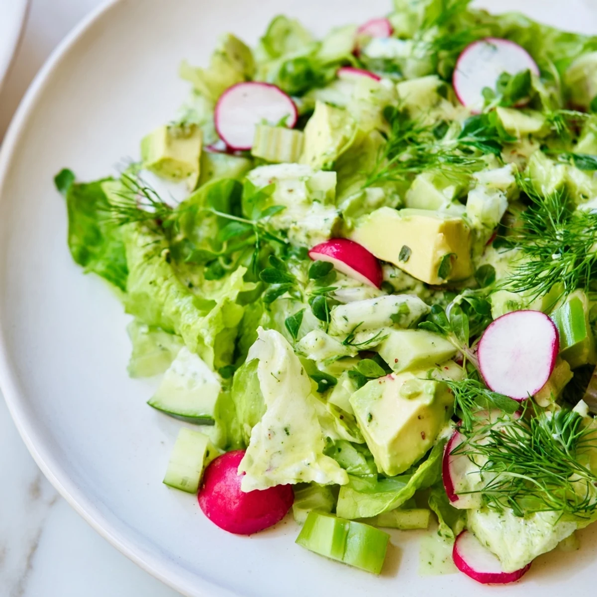 Vibrant Green Goddess Salad with Avocado and Cucumber piled high on a white plate, featuring crisp romaine and creamy diced avocado.  