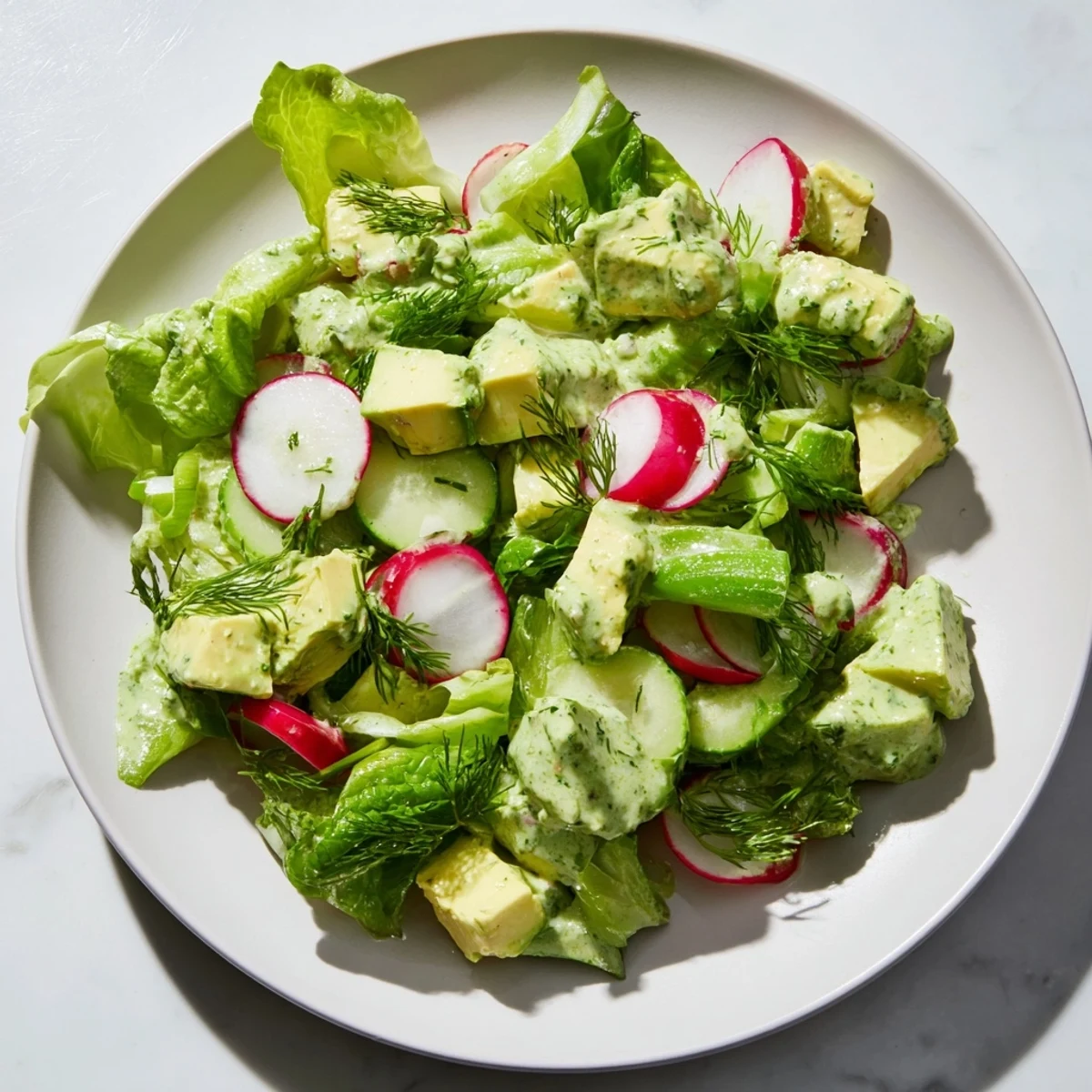 Close-up of a freshly tossed Green Goddess Salad with Avocado and Cucumber, drizzled with herby dressing and topped with radish slices.  