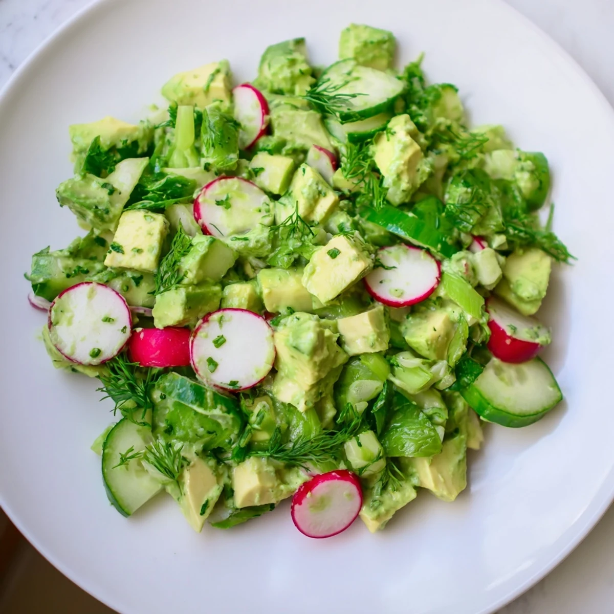 A serving bowl of Green Goddess Salad with Avocado and Cucumber ready for lunch, garnished with fresh dill and parsley.