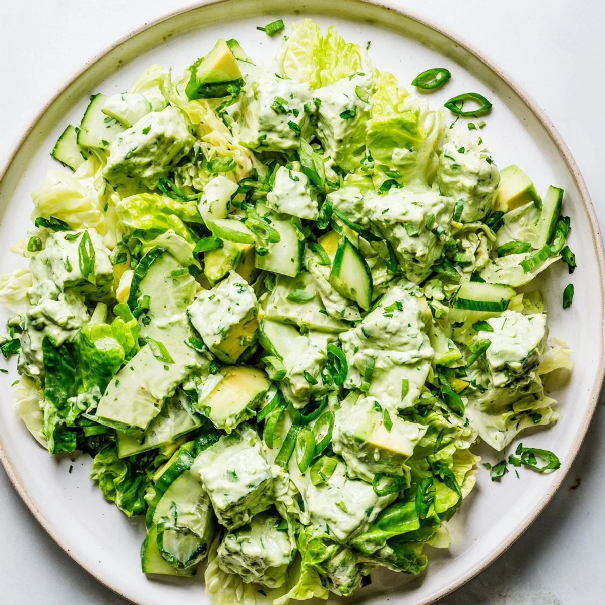 Vibrant Green Goddess Salad topped with diced avocado and herbs on a rustic wooden table.