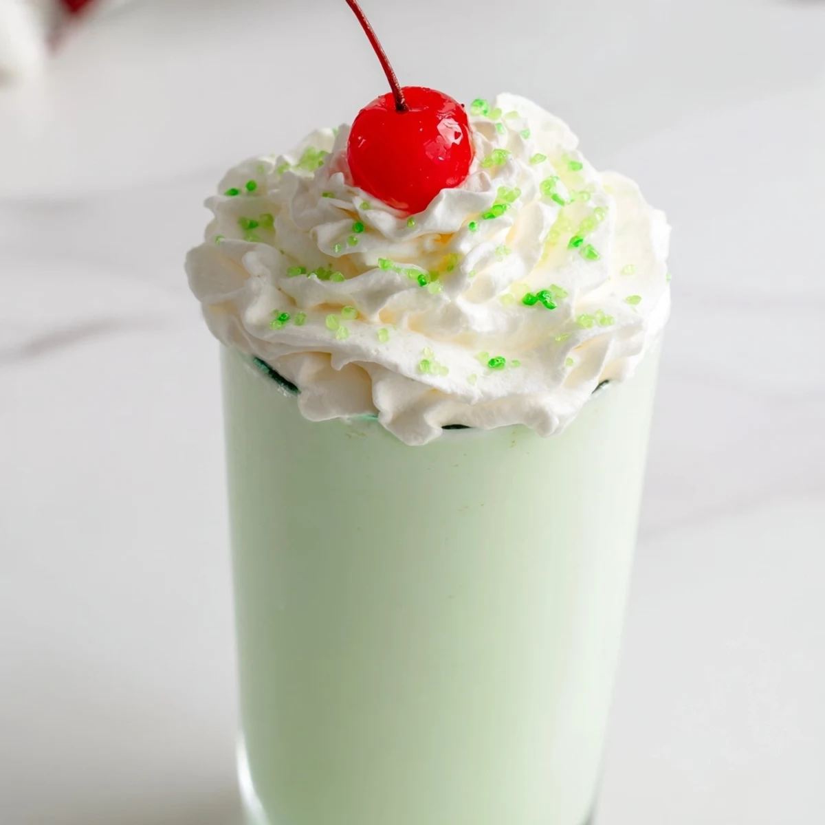 Two tall glasses of creamy Homemade Copycat Shamrock Shake topped with fluffy whipped cream and maraschino cherries, ready to enjoy.