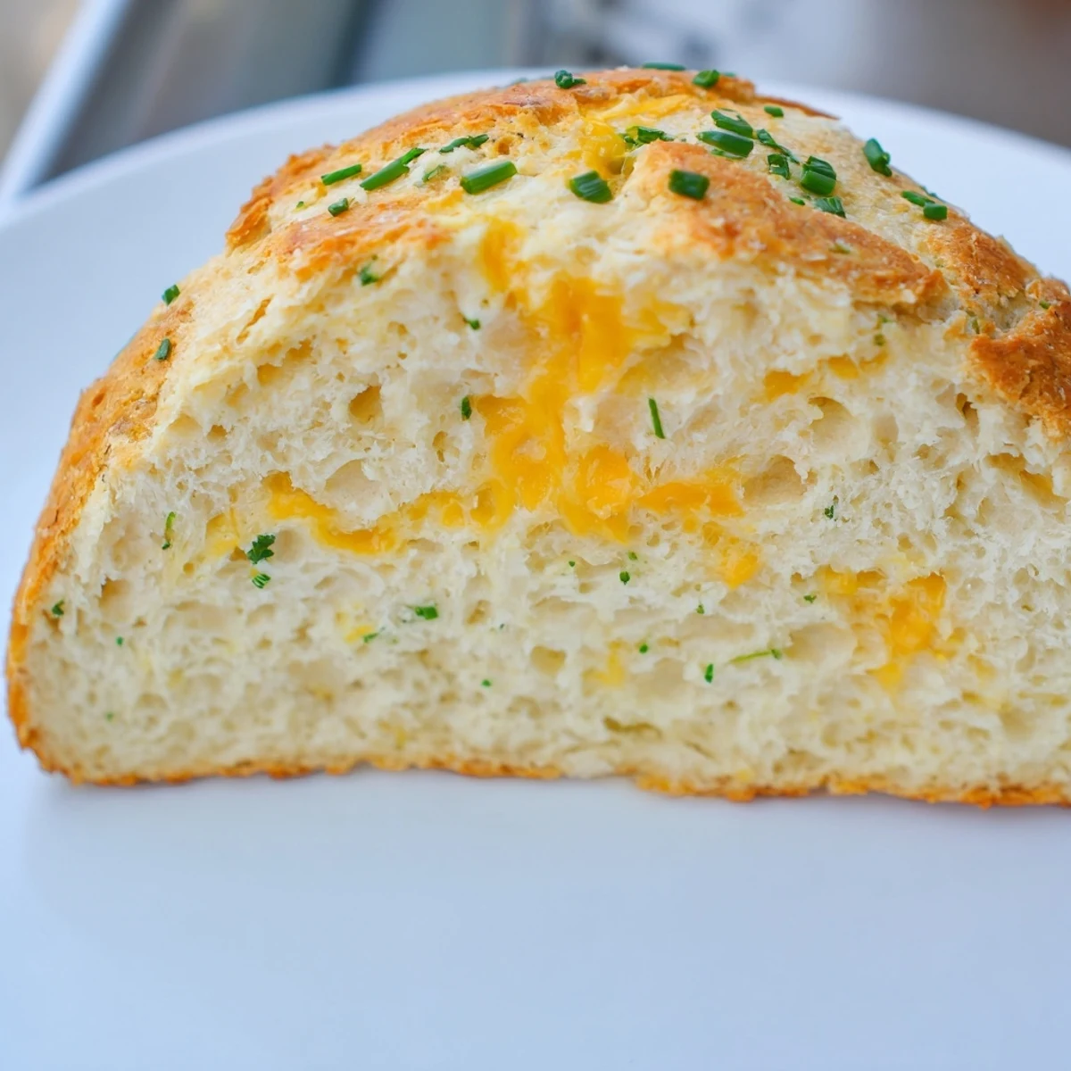 Savory Cheddar & Chive Irish Soda Bread cooling on a wire rack with melted butter on a warm slice nearby.  