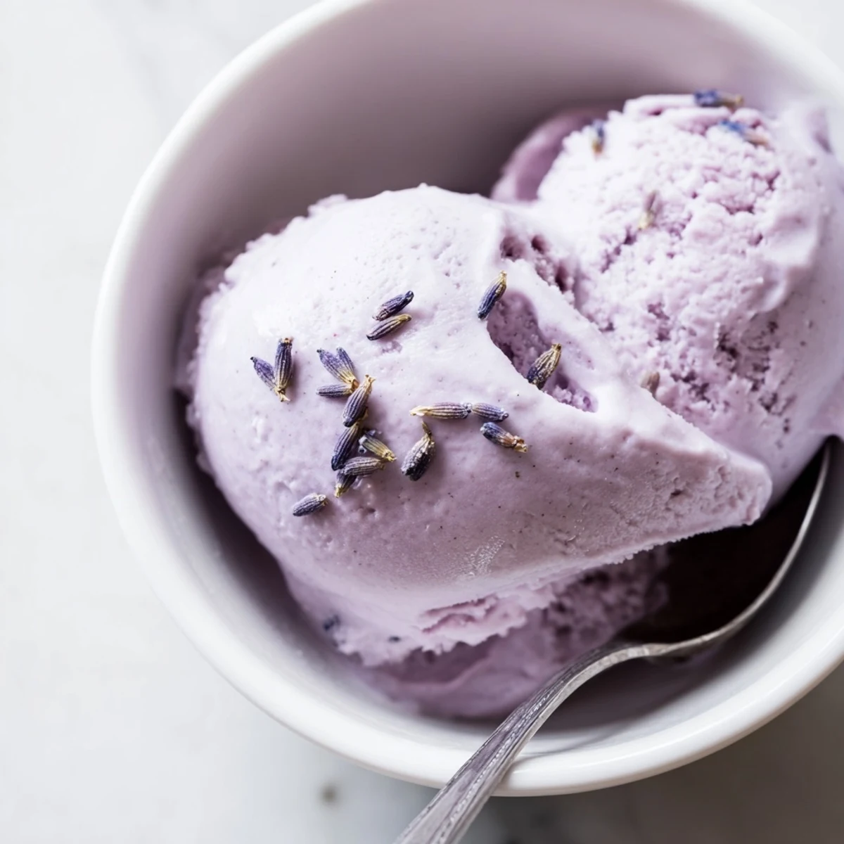 A scoop of Lavender Ice Cream in a rustic bowl, topped with fresh berries and a sprig of culinary lavender, perfect for a summer dessert.