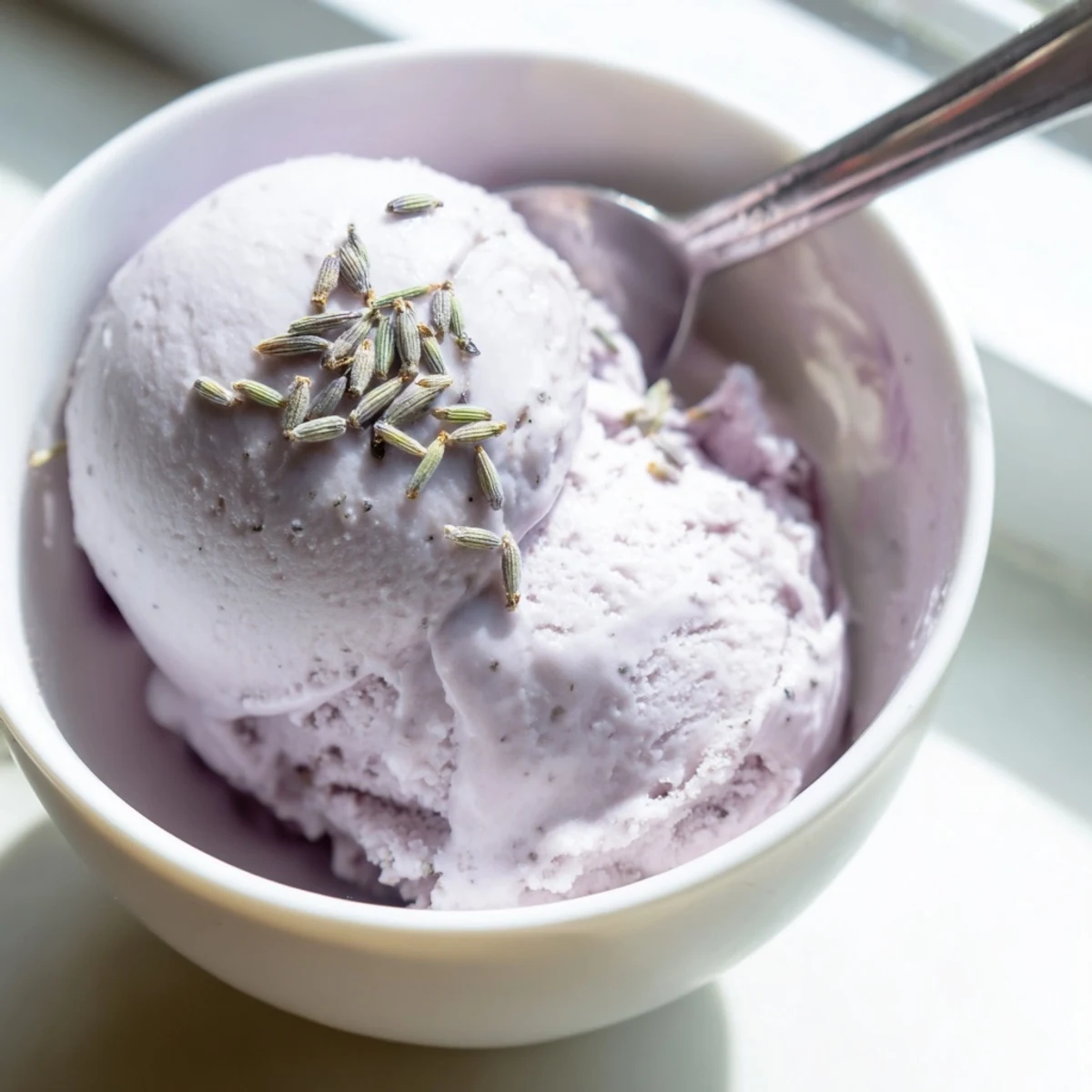 A close-up of Lavender Ice Cream being scooped from a container, showing its creamy texture with flecks of purple floral buds.