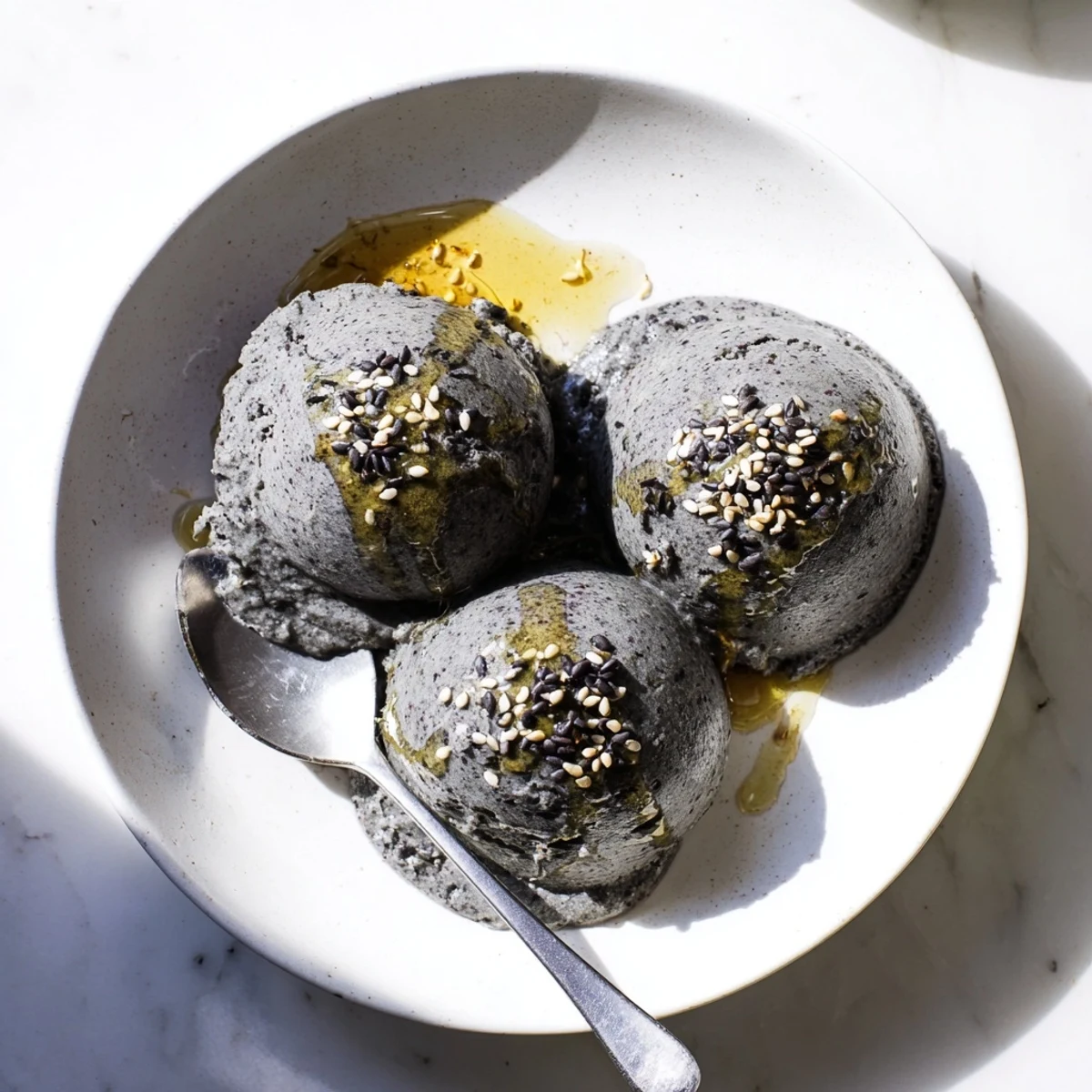A scoop of homemade Toasted Black Sesame Ice Cream in a chilled bowl, garnished with sesame seeds and honey.