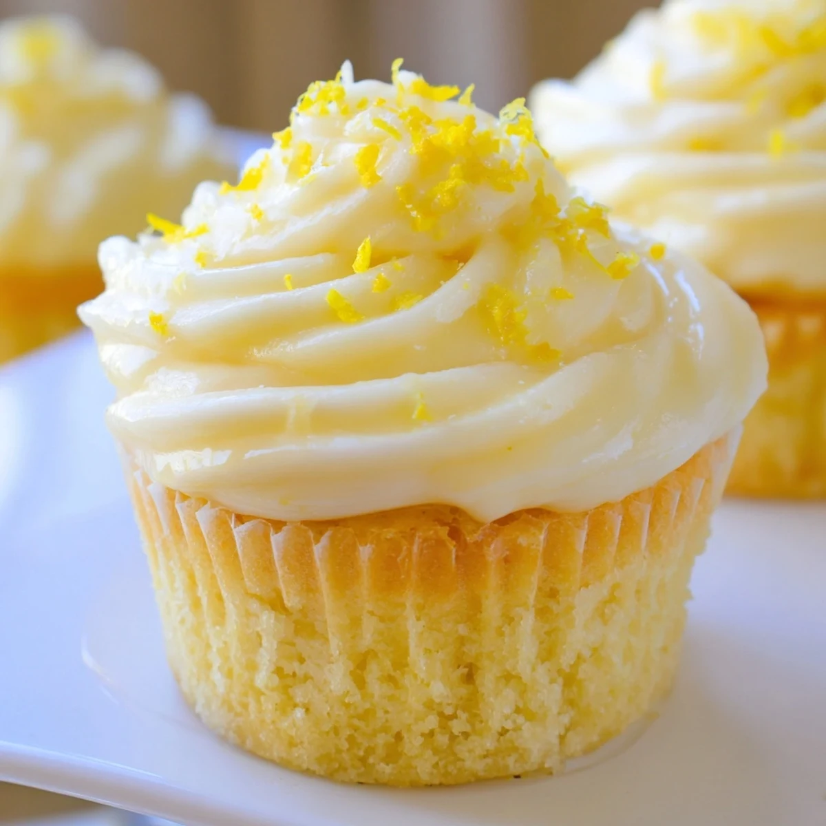 Freshly baked Limoncello cupcakes with fluffy frosting and lemon zest garnish on a marble surface.