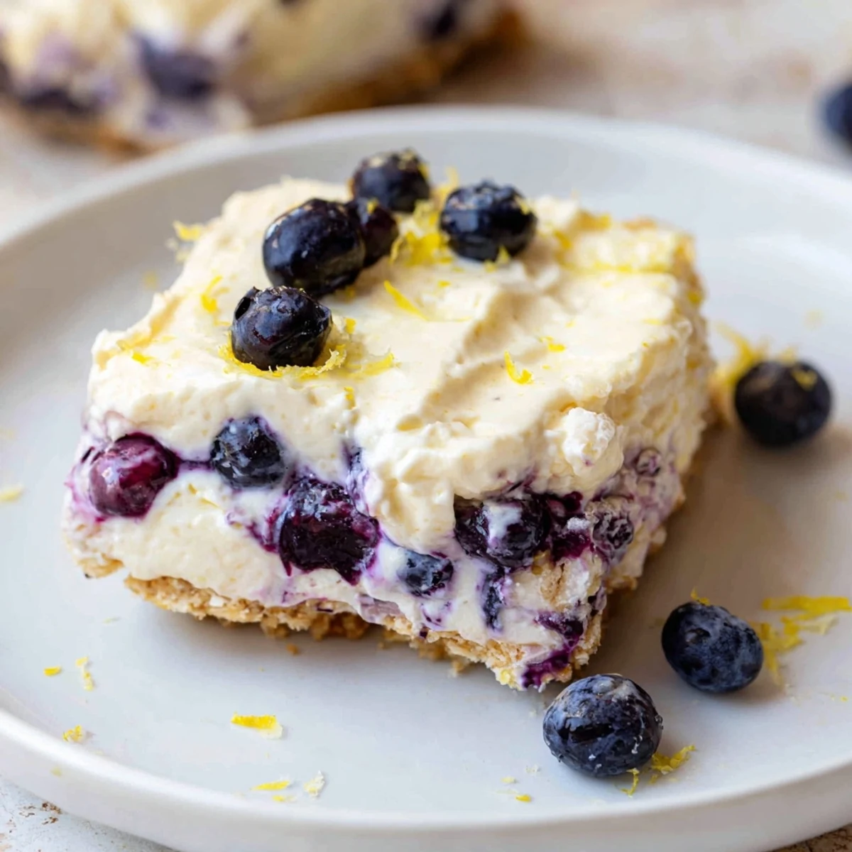 A springform pan reveals layers of No Bake Lemon Blueberry Cream Cake, with light whipped cream and bright lemon zest garnish.