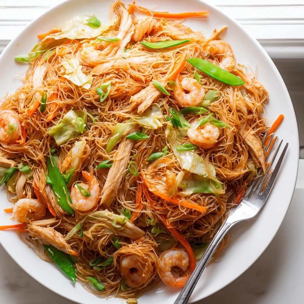 Golden mounds of Traditional Pancit Bihon topped with vibrant vegetables, chicken, shrimp, and fresh scallions on a rustic platter