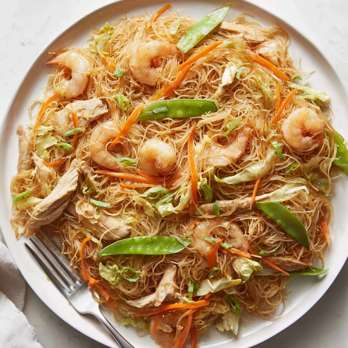 Family-style serving of Traditional Pancit Bihon garnished with green onions and served alongside bright lemon wedges for squeezing