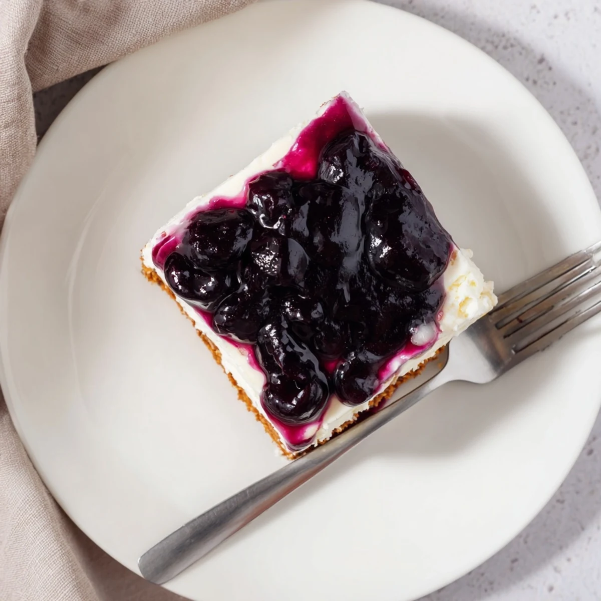 Creamy blueberry cheesecake slice topped with vibrant purple berry compote on white plate