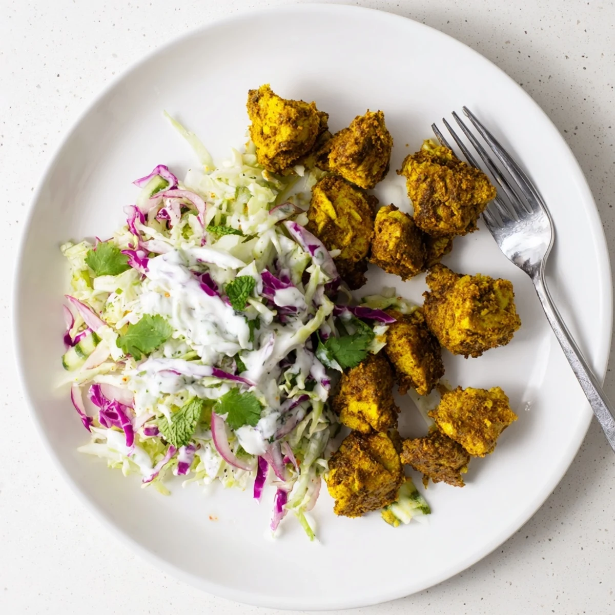 Golden curried chicken slices resting on vibrant purple and green lime coleslaw with creamy mint yogurt drizzle