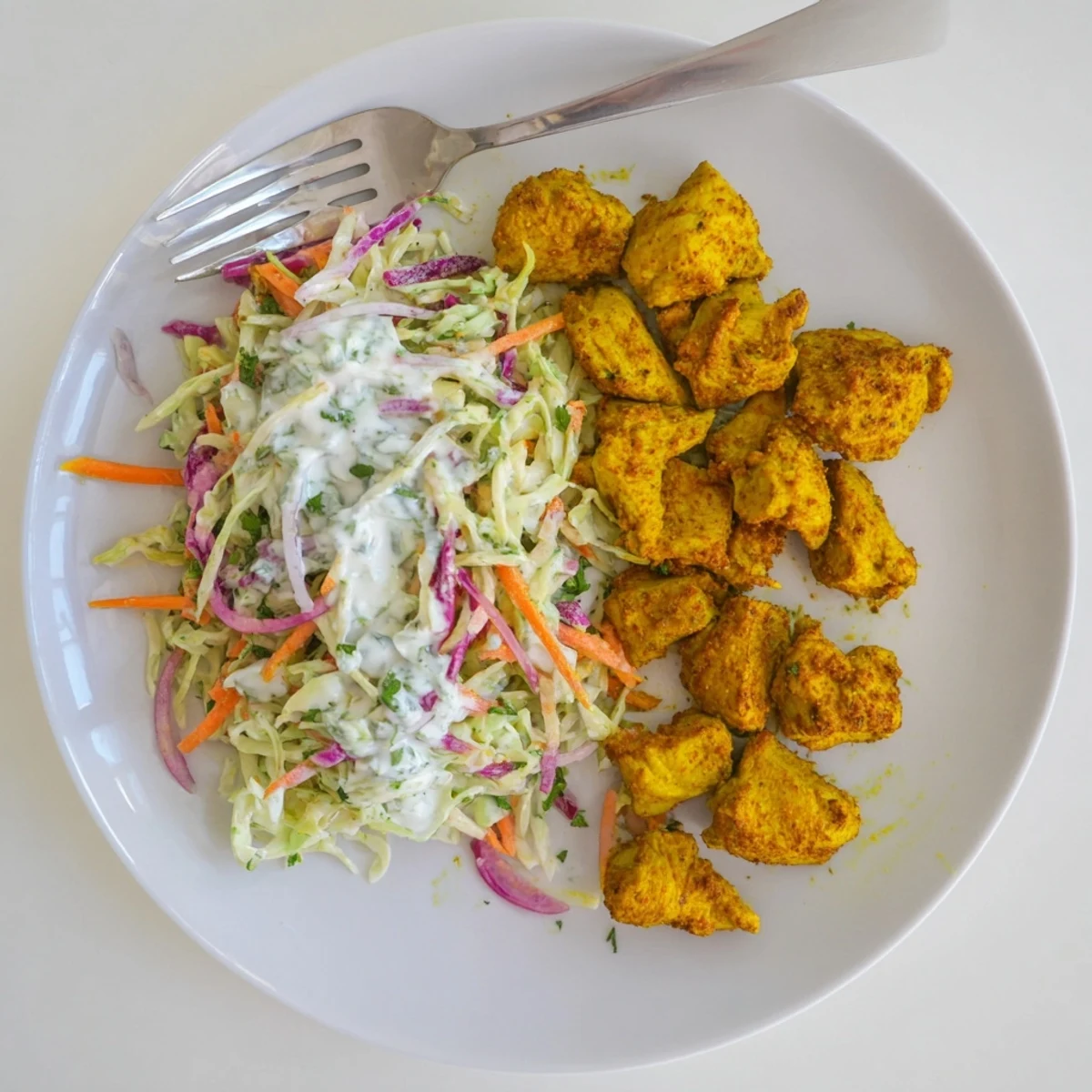 Sliced spiced curry chicken arranged over colorful crisp cabbage slaw topped with refreshing mint yogurt sauce