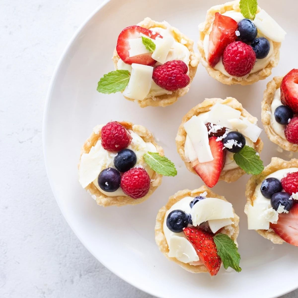Silky white chocolate mousse nestled in delicate tart shells with colorful berries and mint garnish