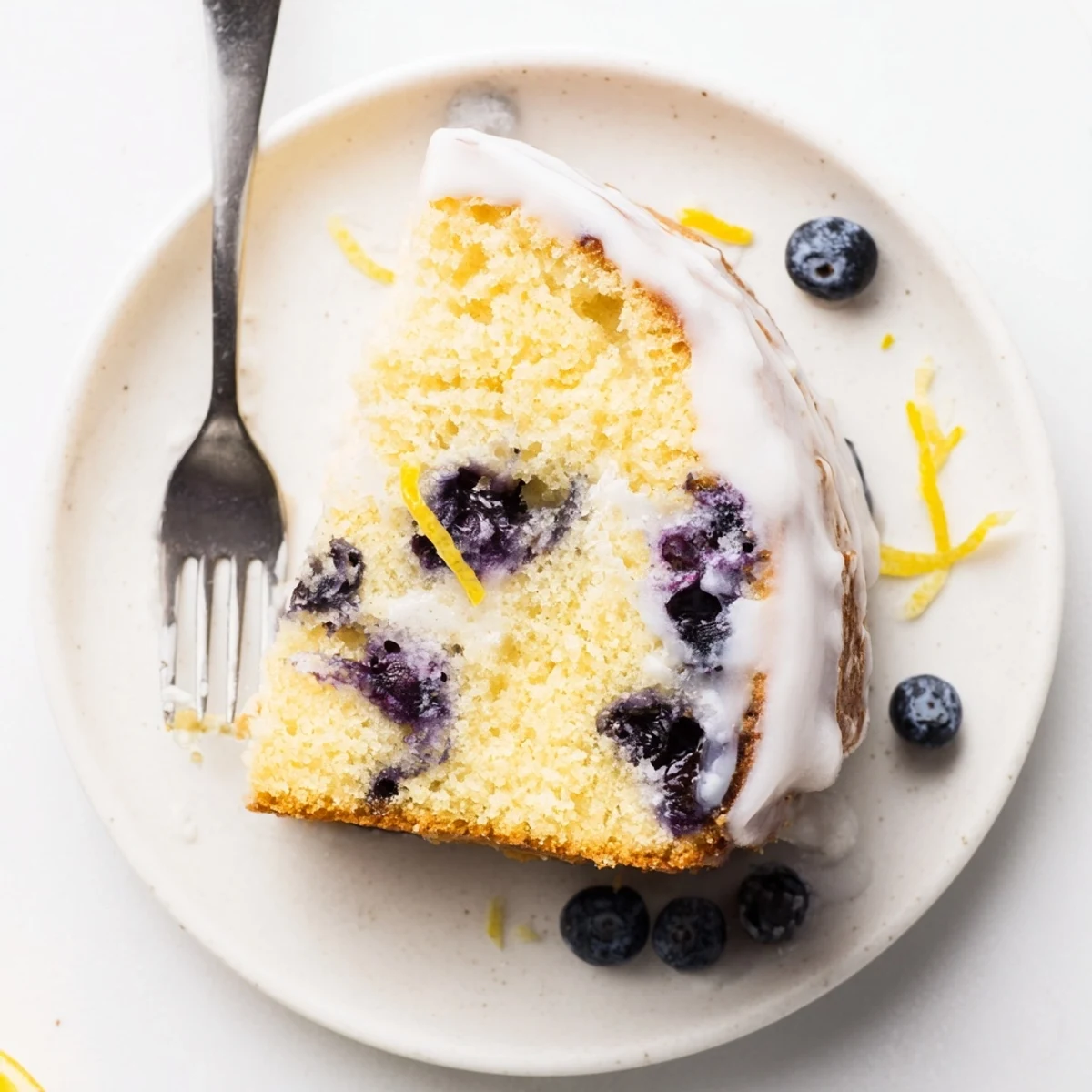 Beautiful lemon blueberry cake with zesty glaze on a white serving plate with fresh berries