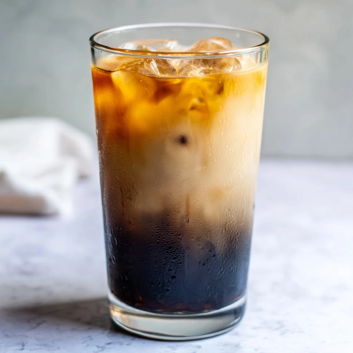 Tall chilled glass of sweet Okinawa milk tea topped with white milk foam