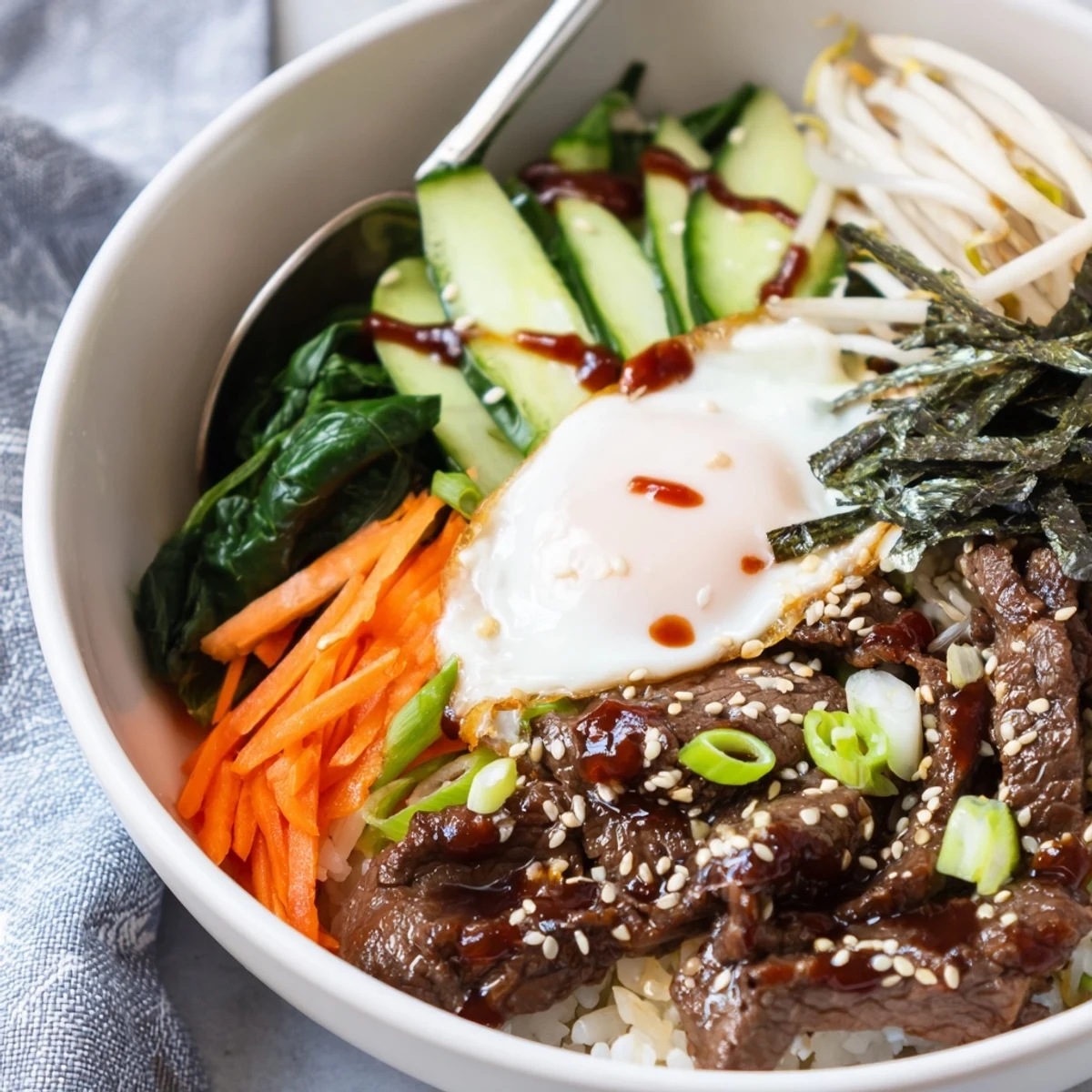 Vibrant Korean-inspired breakfast bowl arranged with beef, colorful veggies, and golden yolk on white rice