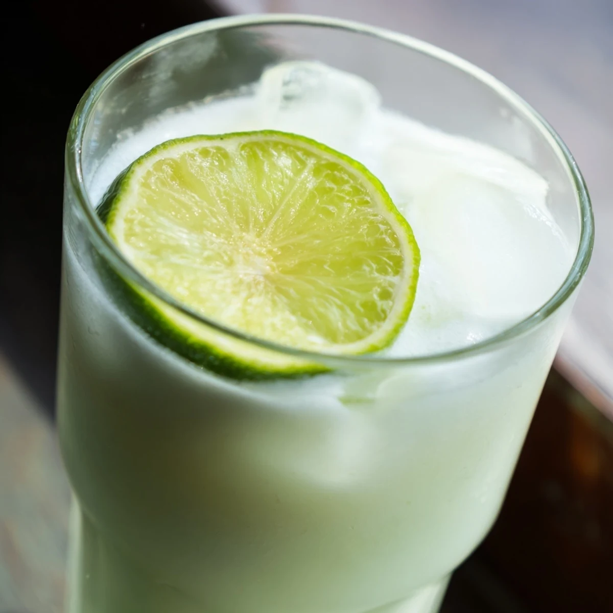 Pitcher of pale green creamy Brazilian lemonade served over ice with lime wheel garnish
