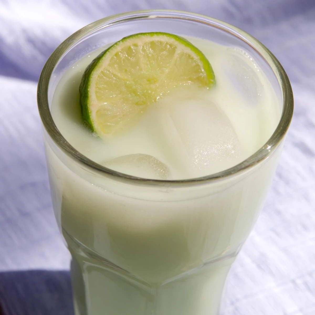 Refreshing creamy Brazilian lemonade poured into glasses with floating lime wedges and ice cubes