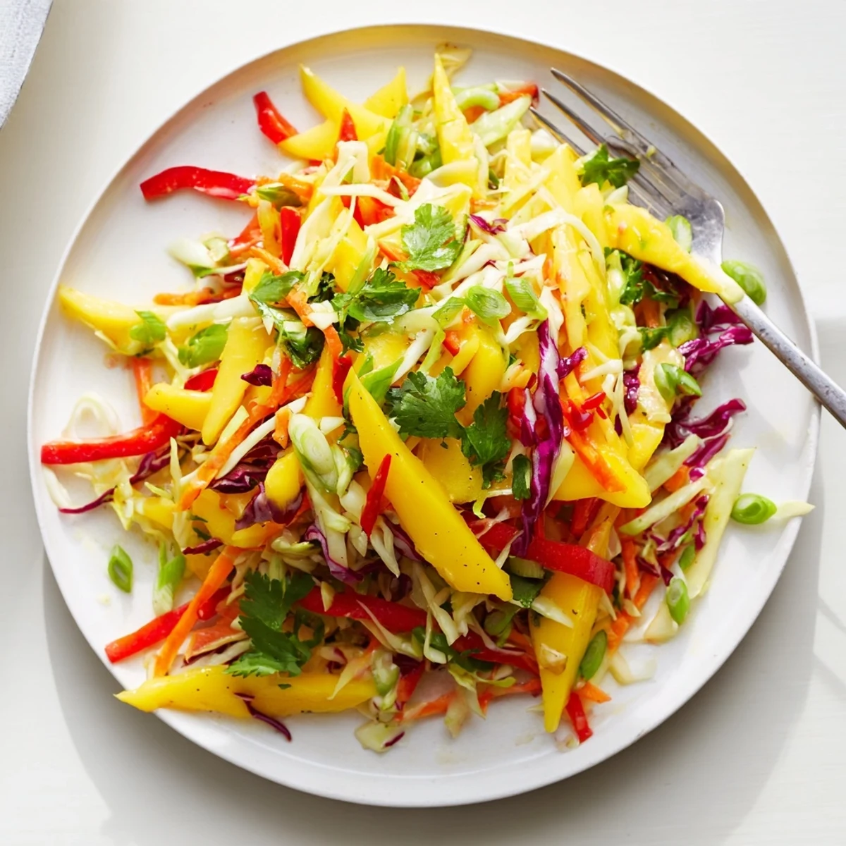 Fresh tropical mango slaw featuring julienned mango, red and green cabbage, carrot, and cilantro in tangy dressing