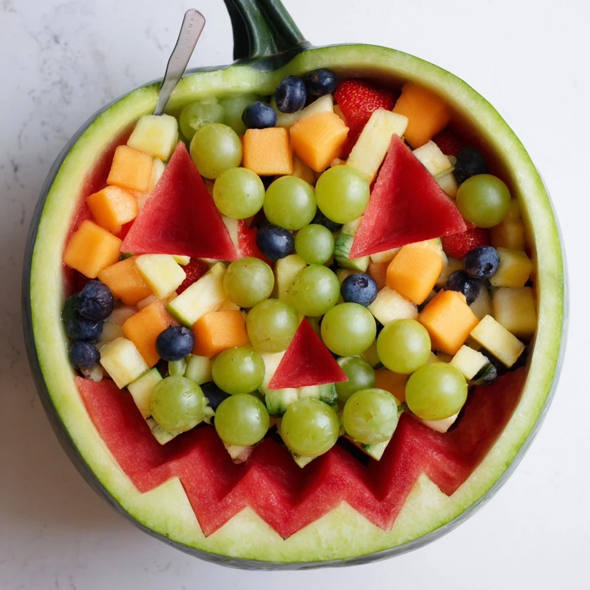 Carved watermelon jack o lantern filled with colorful mixed fruit salad for festive Halloween parties