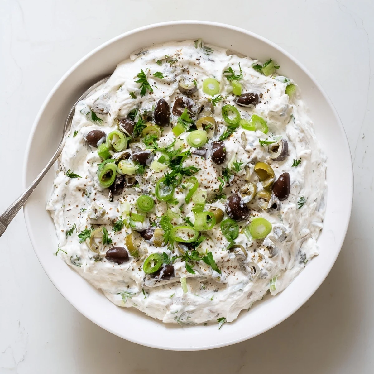 Creamy white olive dip speckled with briny black and green olives served in a ceramic bowl
