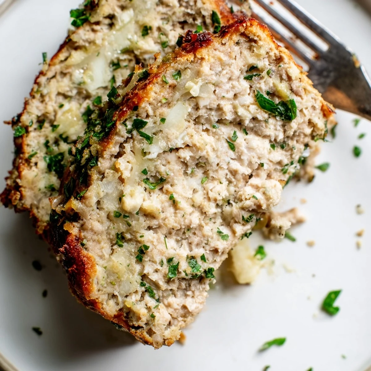 Golden-topped garlic parmesan chicken meatloaf sliced on a white serving platter