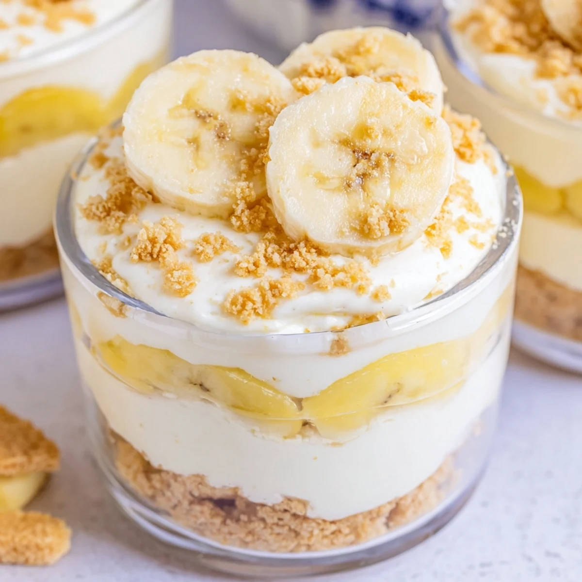 Individual no bake banana pudding cheesecake cups topped with whipped cream and crunchy cookie crumbles