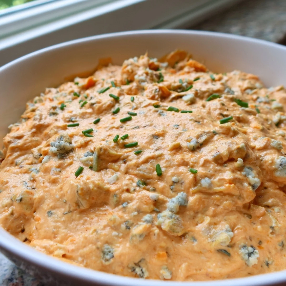 Creamy buffalo pickle dip in a serving bowl surrounded by crispy chips and fresh veggie sticks ready for dipping