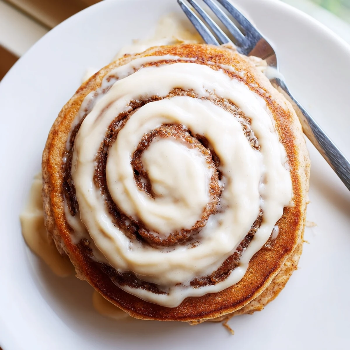 Golden cinnamon roll pancakes drizzled with creamy cream cheese icing on a warm plate