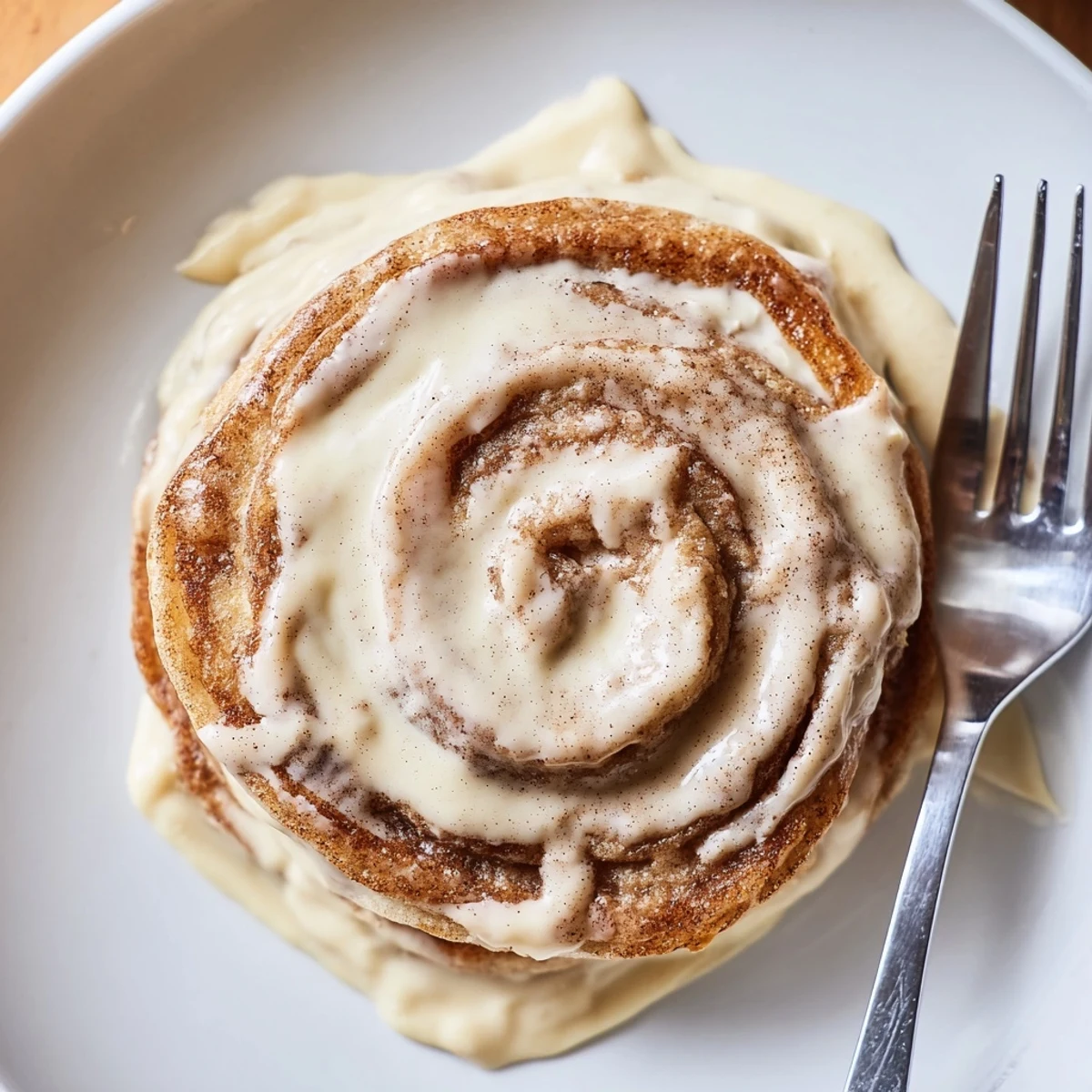 A stack of warm cinnamon roll pancakes oozing rich cinnamon swirl under white glaze