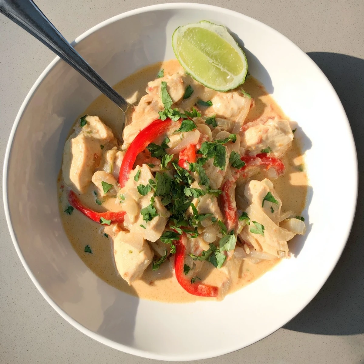 Golden brown chicken thighs simmered in creamy coconut milk sauce with red bell peppers and fresh cilantro garnish