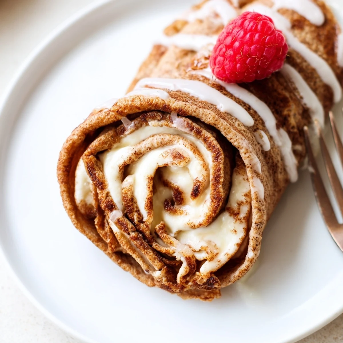 Stack of Cinnamon Roll Protein Crepes Recipe drizzled with protein glaze, berries.